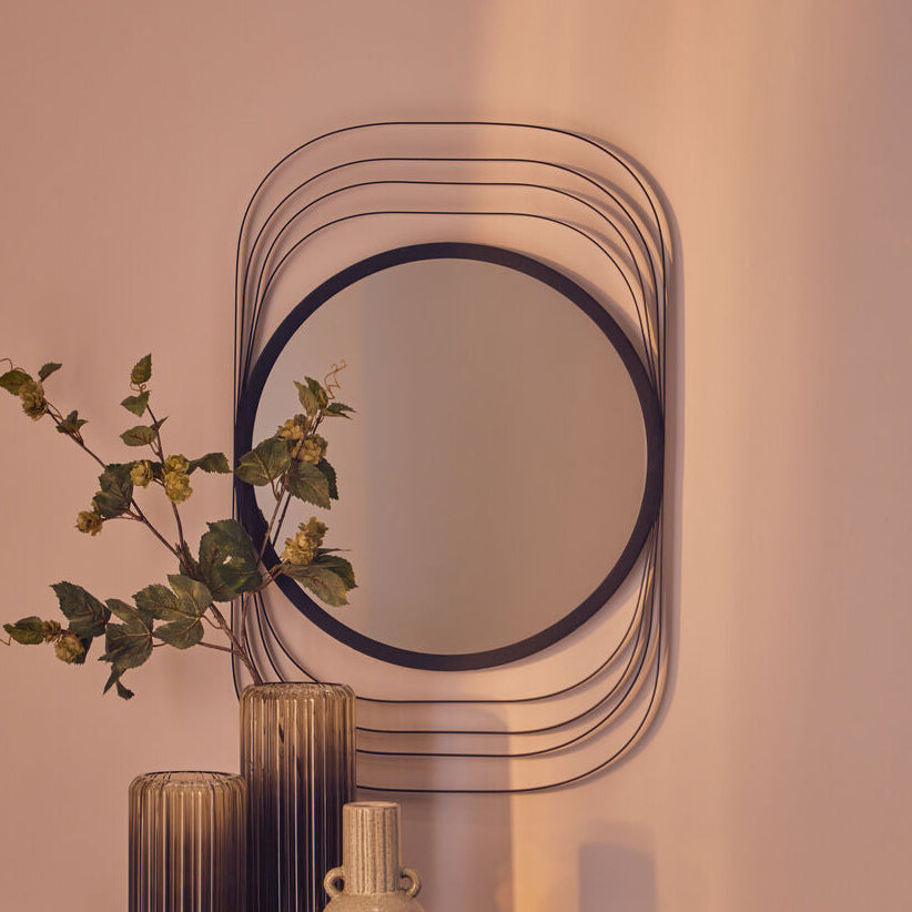 Decorative mirror with a vase and plant on a table against a beige wall