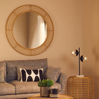 Living room with a gray sofa, round mirror, and wicker coffee table.