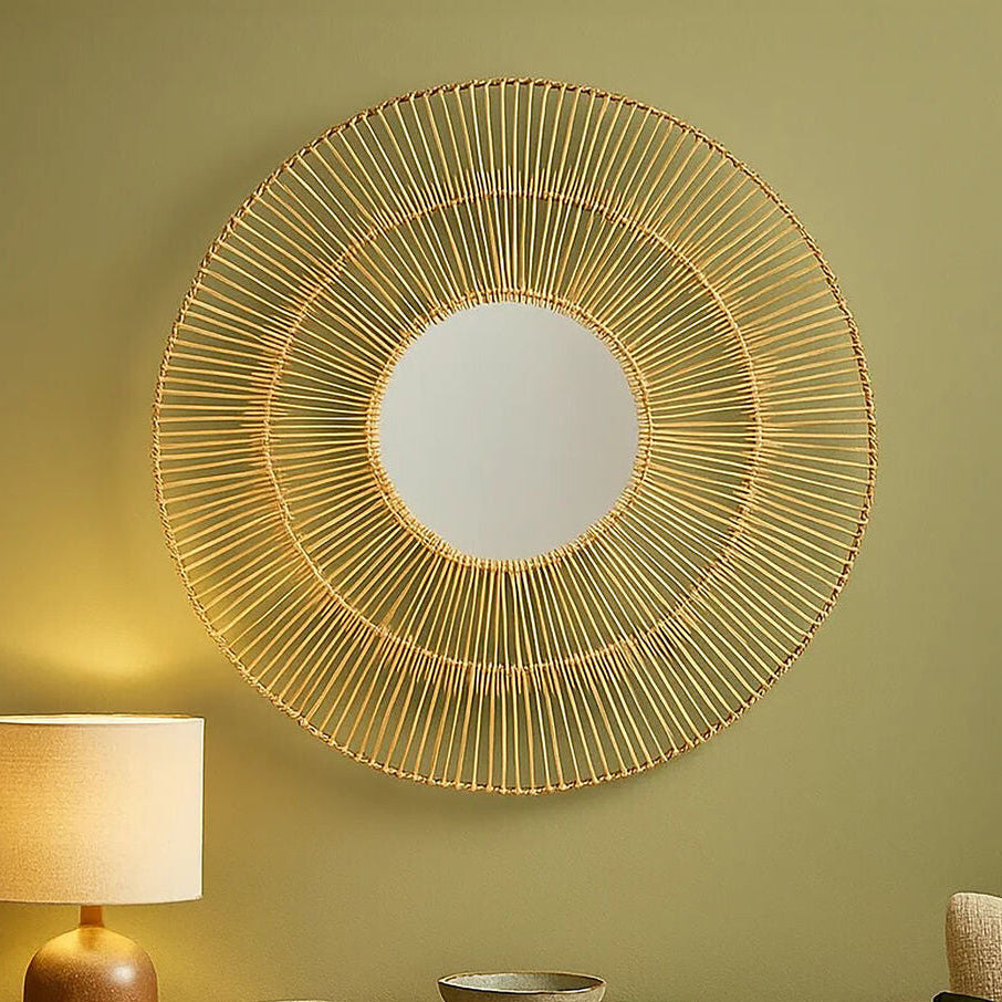 Decorative round mirror with gold wire frame on a green wall above a wooden side table with lamp and bowls.