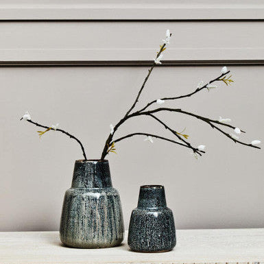 Two dark gray textured vases with branches on a light wooden surface against a neutral background