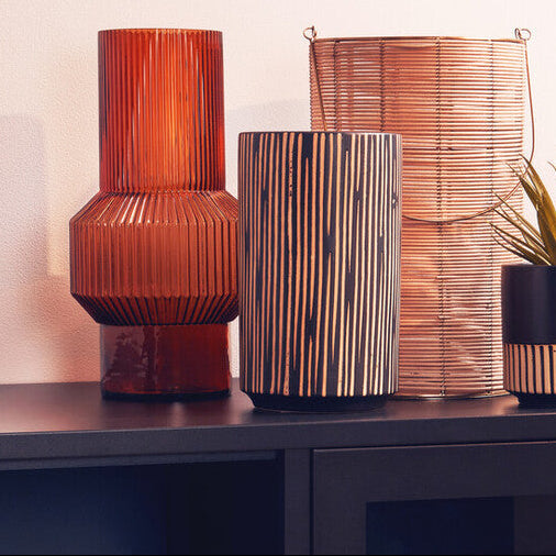 Decorative vases and a plant on a black cabinet against a light wall.