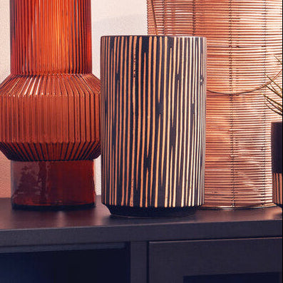 Decorative vases and a plant on a black cabinet against a light wall.