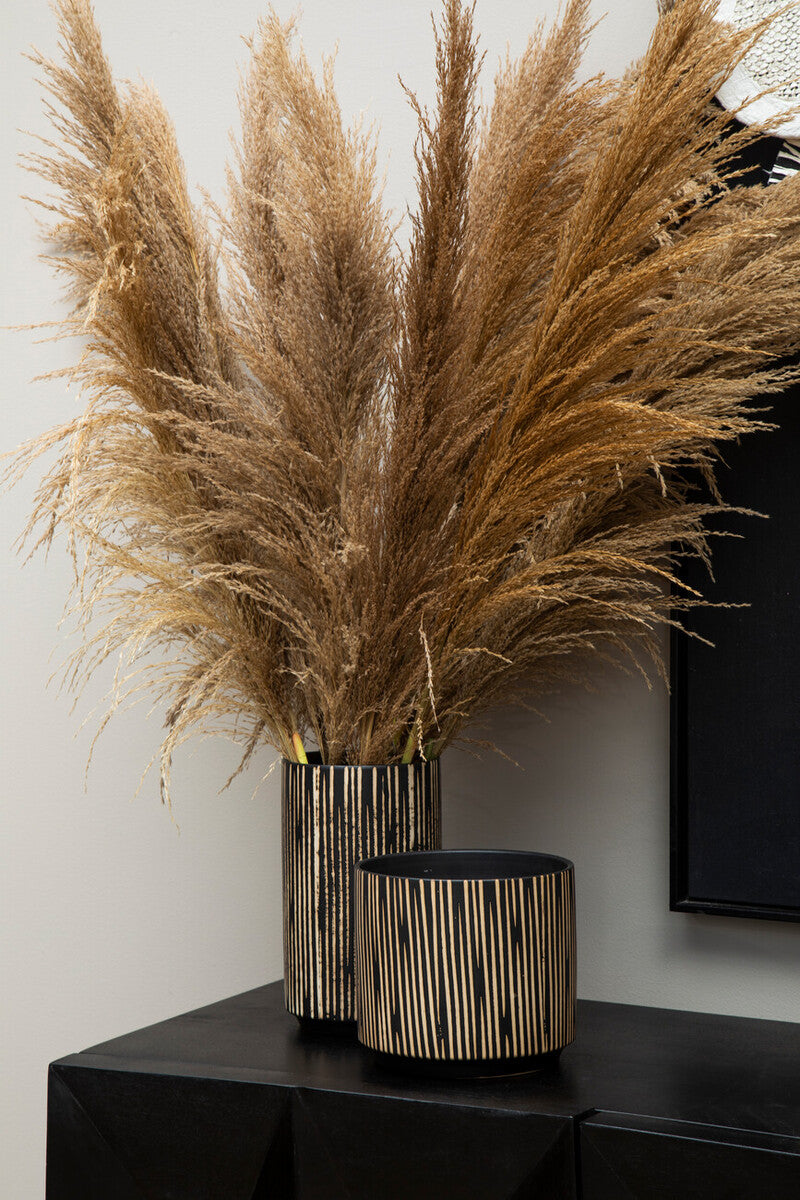 Decorative arrangement of dried pampas grass in a metallic vase on a black surface.