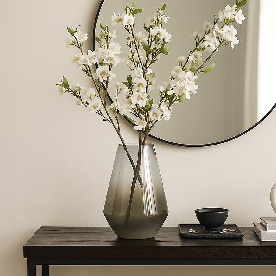 Round mirror above a console table with a vase of flowers, books, and a decorative object.