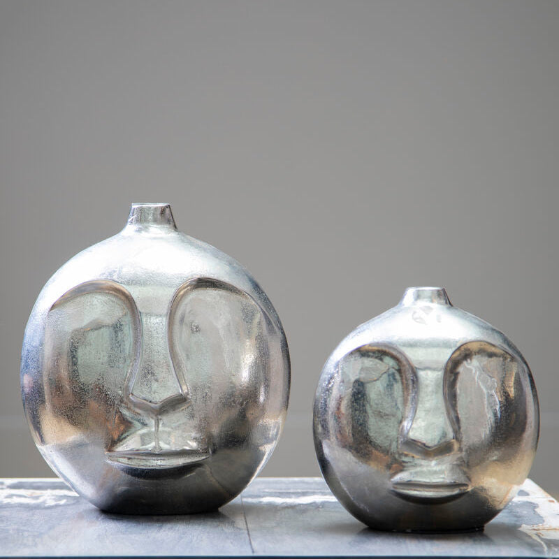 Two silver face-shaped vases on a marble surface with a gray background