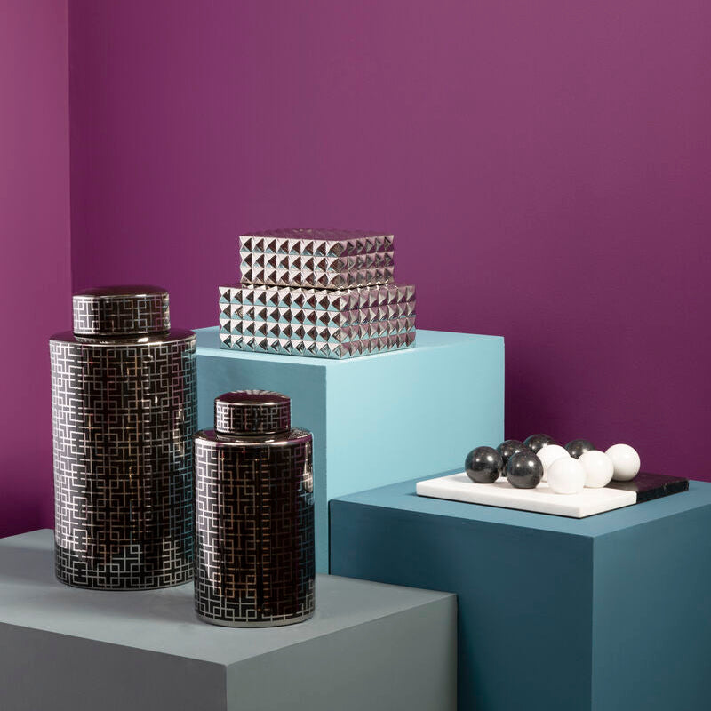 Decorative vases and sculptures on geometric platforms against a purple wall