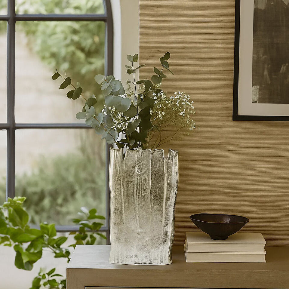 Decorative vase with greenery on a wooden surface next to a window