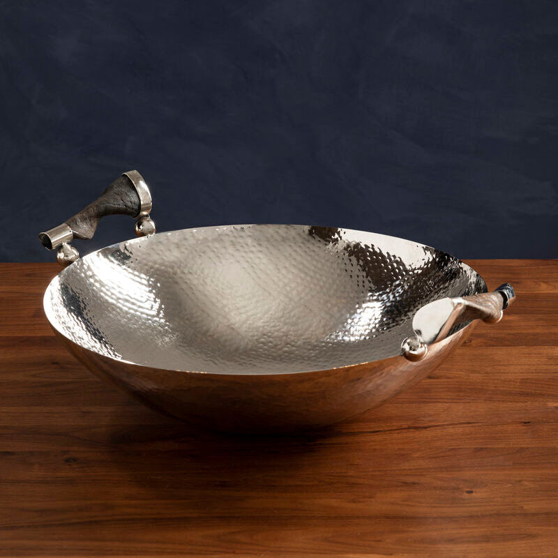 Silver hammered bowl with handles on a wooden surface against a dark background
