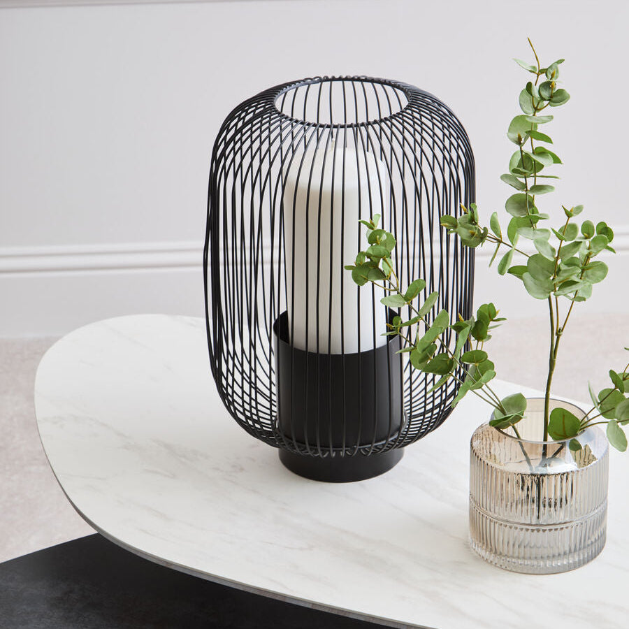 Black wire cage lamp on a white table with a plant