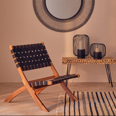 Round woven mirror above a chair with a side table and decorative items in a room.