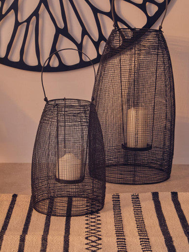 Two black wire mesh lanterns on a striped surface with a decorative wall in the background.