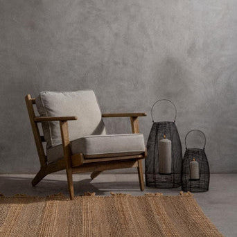 Wooden armchair with a gray cushion against a gray wall with two black lanterns on a rug.