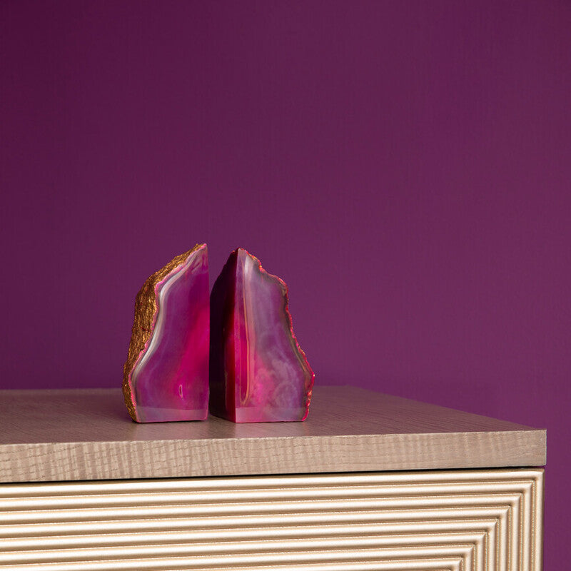 Pink agate bookends on a textured surface with a purple background