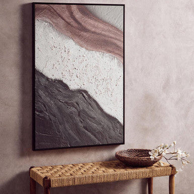 Abstract art piece on a wall above a woven bench with a bowl and flowers.