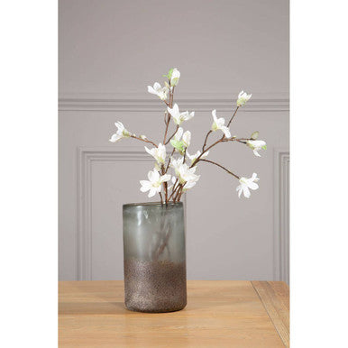 Decorative vase with white flowers on a wooden surface against a gray wall.