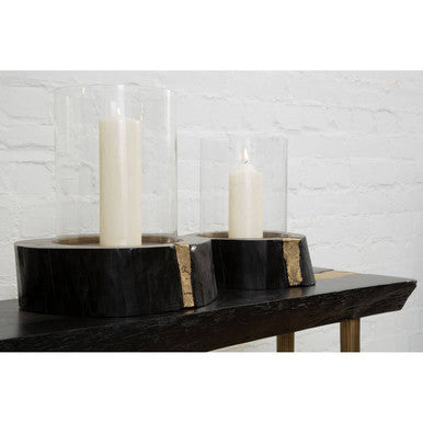 Two candle holders with candles on a wooden surface against a white brick wall.