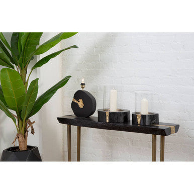 Decorative items on a black console table with a plant and white brick wall in the background