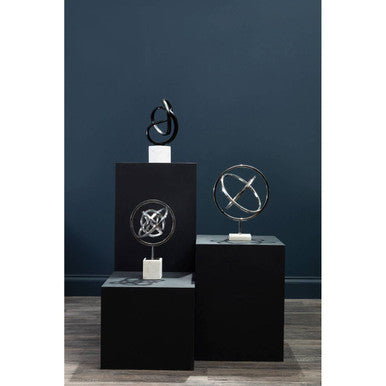 Three abstract sculptures on black pedestals against a dark blue wall.