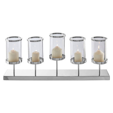 Five glass candle holders with candles on a reflective surface