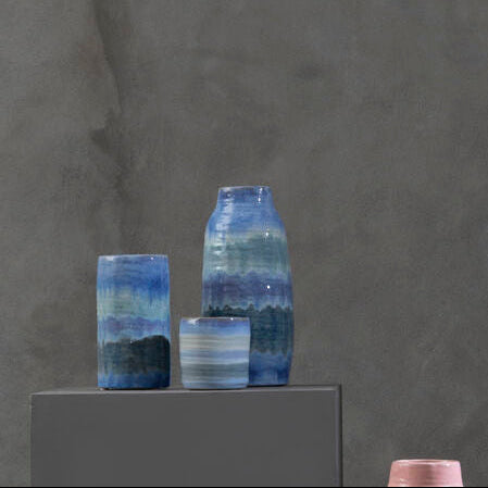 Vases with gradient colors on gray pedestals against a dark gray background