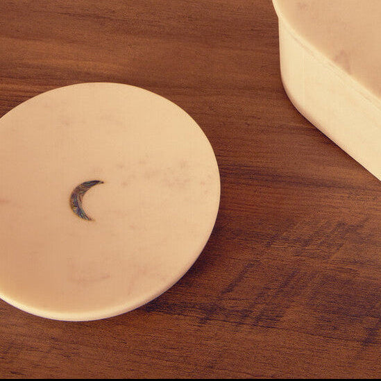 Decorative items on a wooden surface including a cylindrical box, a round coaster, and a small cup.