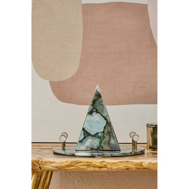 Marble triangle sculpture on a wooden surface with a lamp in the background