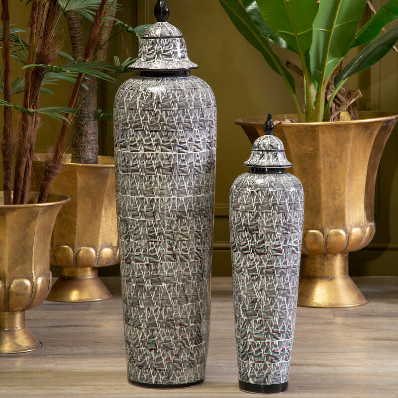 Two decorative vases with intricate patterns on a wooden surface with plants in the background.