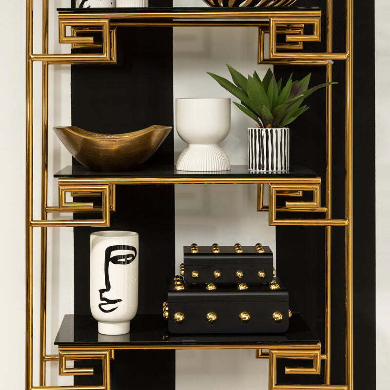 Decorative shelf with gold frame and black and white decor items against a black and white striped wall.