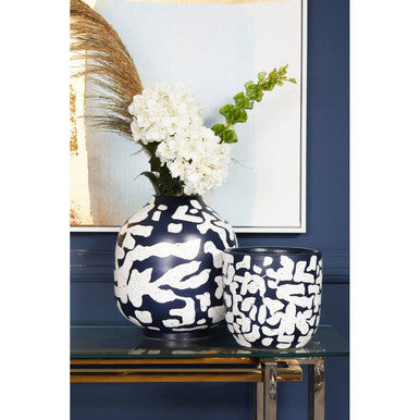 Two black and white patterned vases on a glass table with a blue wall and framed picture in the background.