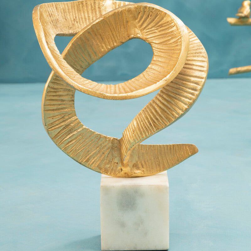Gold abstract sculpture on a white marble base against a teal background