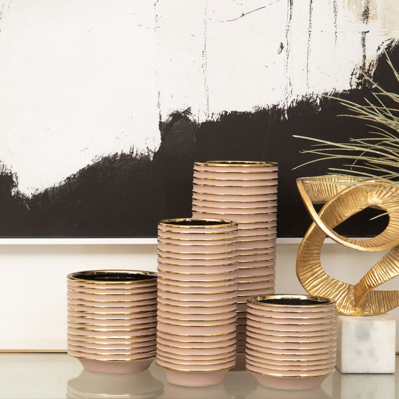 Stacked ceramic pots with gold accents on a white surface against a black and white abstract painting.