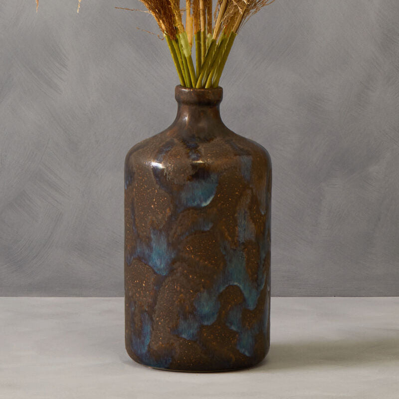 Brown ceramic vase with blue glaze holding dried pampas grass against a gray background