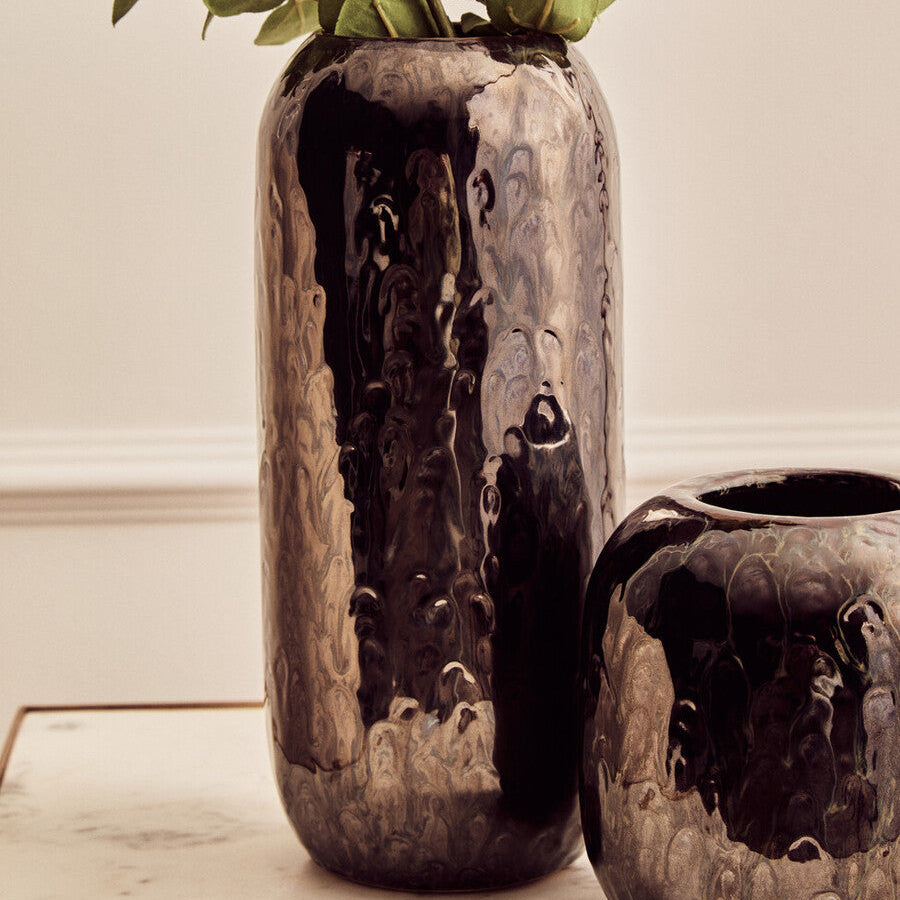 Two rustic ceramic vases with textured surfaces and green leaves on a light background