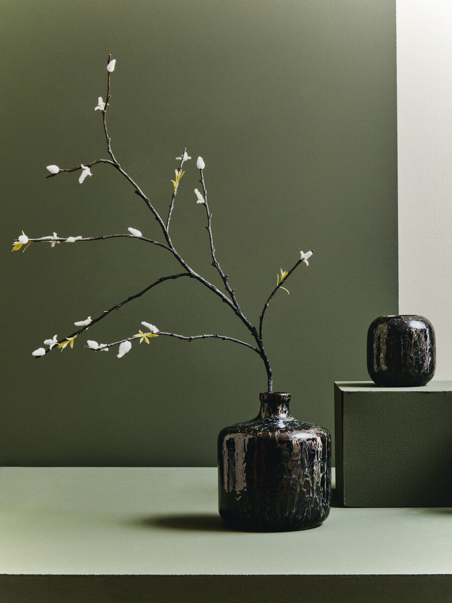 Dark brown vase with branches on a green surface against a green wall