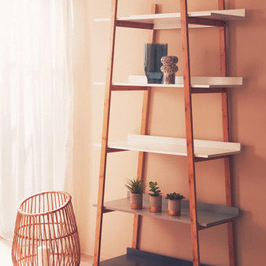 Wooden ladder shelf with white shelves against a beige wall, featuring decorative items and a woven basket.