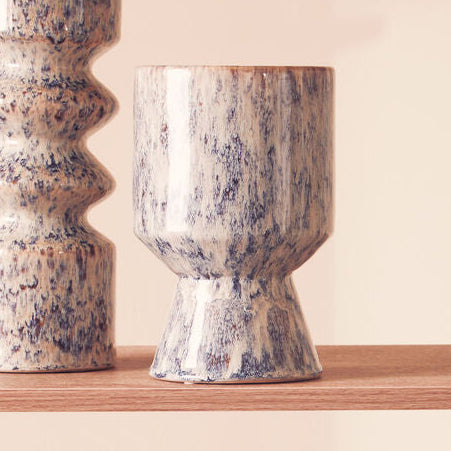 Two ceramic vases with a speckled pattern on a wooden shelf against a beige background