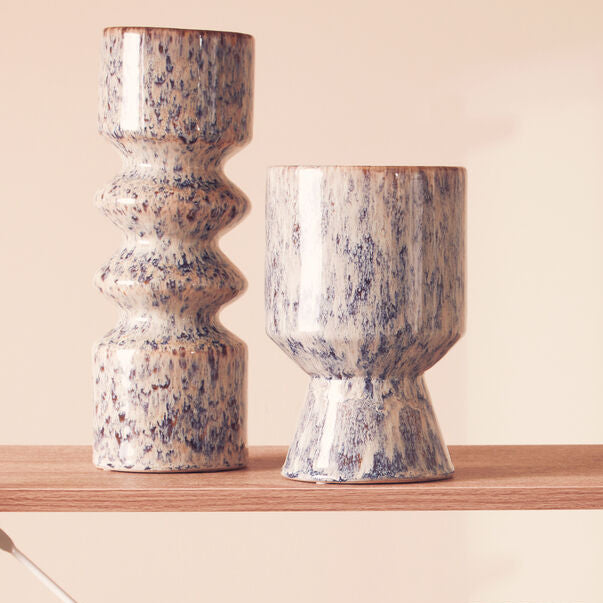 Two ceramic vases with a speckled pattern on a wooden shelf against a beige background