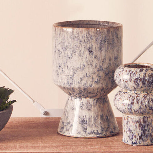 Set of ceramic vases and a bowl with plants on wooden shelves against a beige wall.