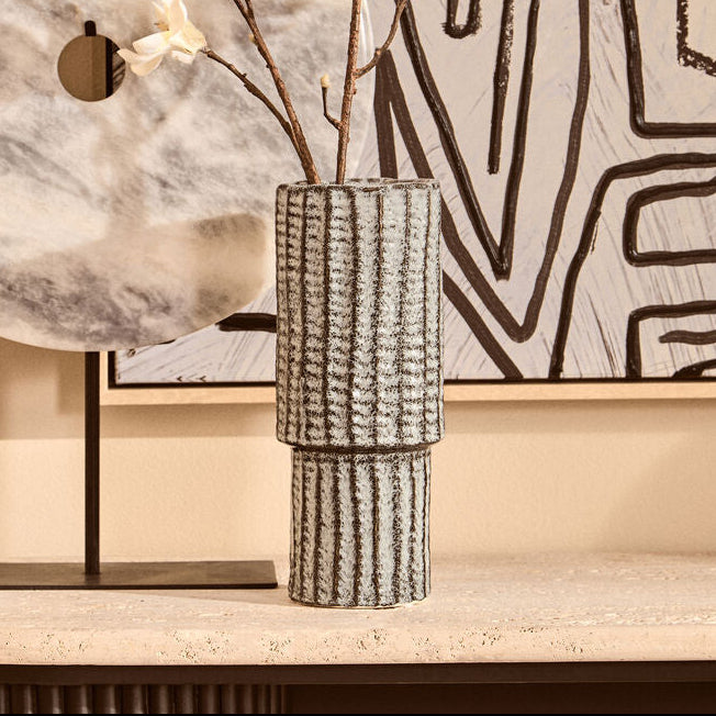 Decorative setup with a marble-patterned lamp, vase with branches, and abstract wall art.