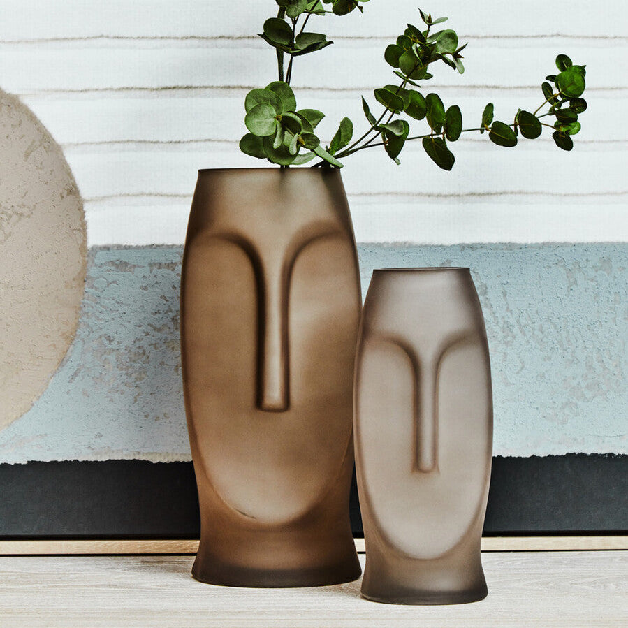 Two face-shaped vases with greenery on a wooden surface