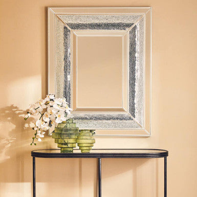 Console table with decorative mirror and flowers against a beige wall