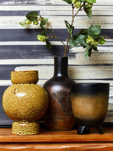 Three ceramic vases on a wooden surface with a striped wall in the background
