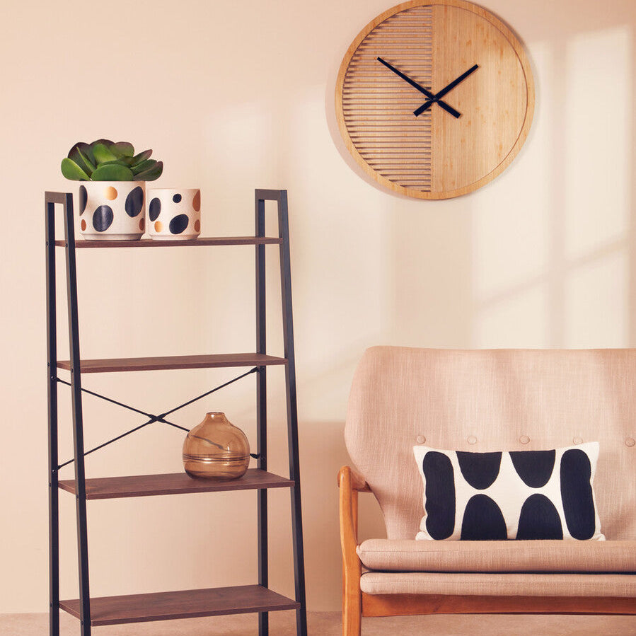Living room with a shelf, plant, clock, and sofa with a pillow.