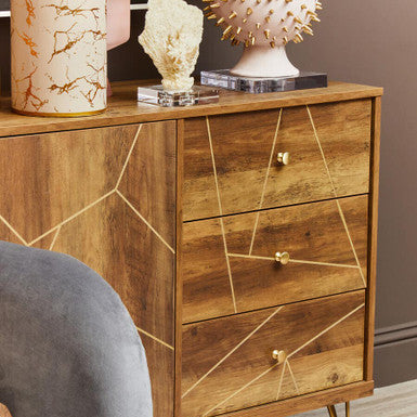Wooden dresser with gold accents and decorative items on top, next to a gray armchair.