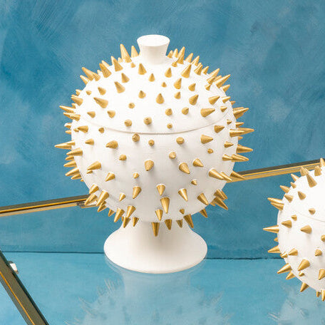 Glass table with gold frame displaying two decorative white urns with spiky textures on a blue background.