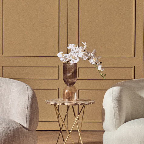 Two beige armchairs in a room with wooden paneling and a small table with flowers.