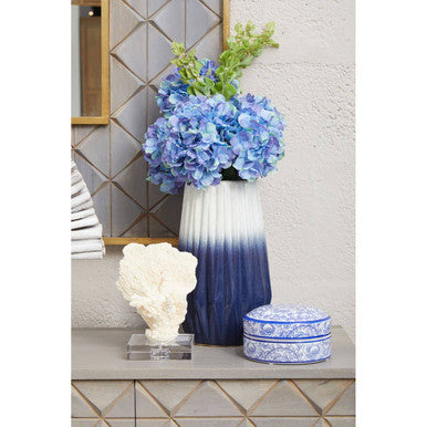 Decorative vase with blue and white gradient, surrounded by flowers and decorative items on a table.