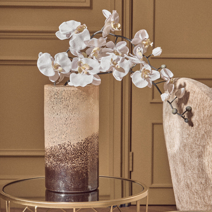 Decorative vase with white flowers on a gold table against a brown paneled wall.