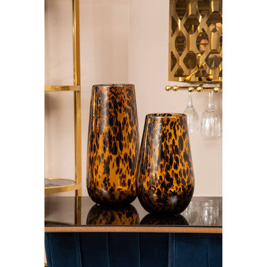 Two tortoiseshell patterned vases on a reflective surface with a decorative wall in the background.