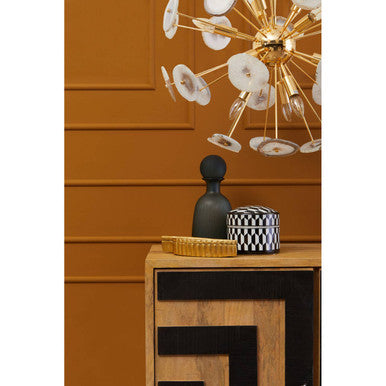Decorative table with a black vase, woven basket, and patterned container against a wooden panel wall.